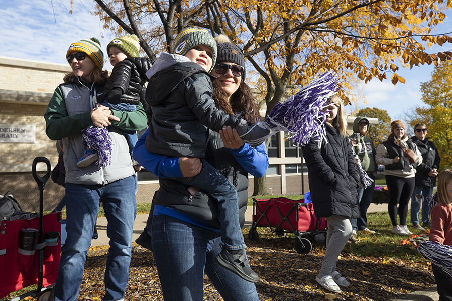 Two parents hold small children in their arms and wave a purple and white pom pom.