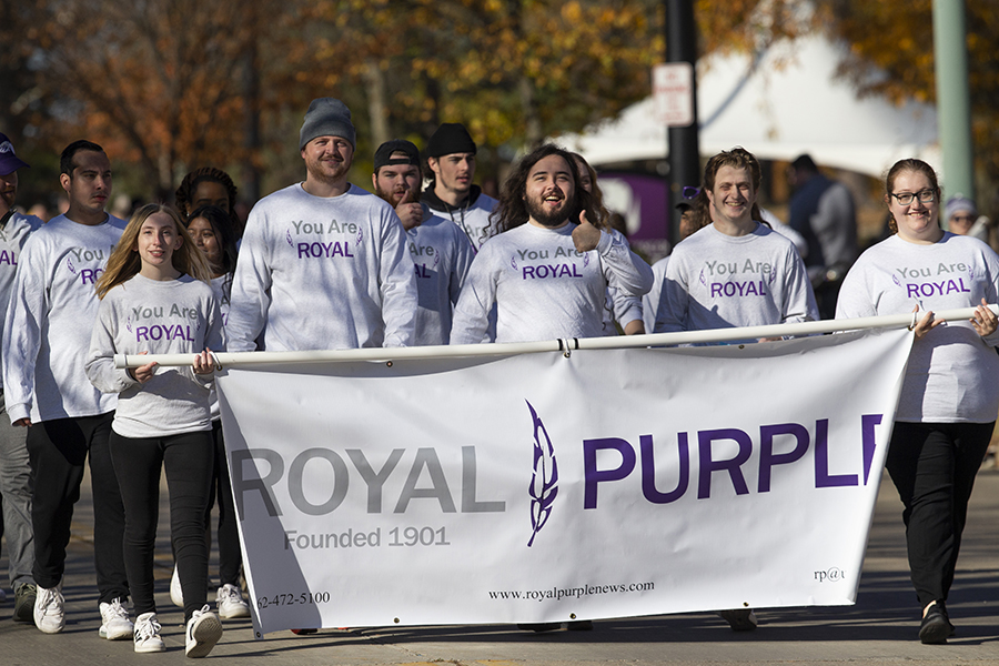 Students walk in a parade holding a white banner that says Royal Purple.