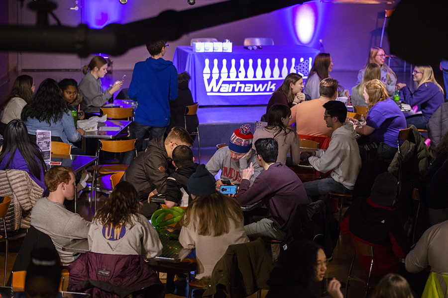Students sit at tables with neon lights in the background.