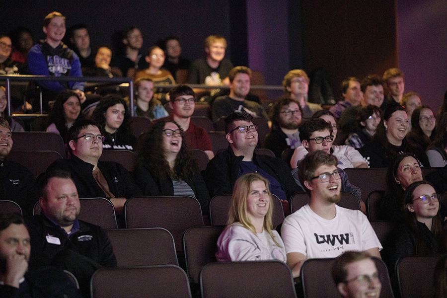 Students laugh as they watch a movie and sit in theatre-style seating.