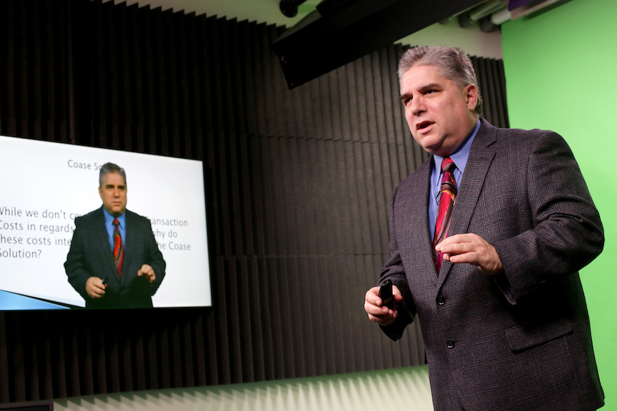 Image: Professor standing in front of a gren screen super imposed onto a powerpoint slide.