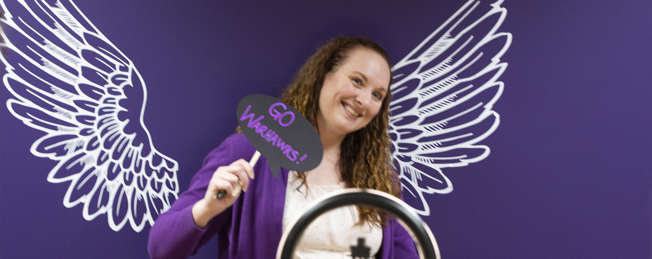Person stands in front of a purple background with white wings.