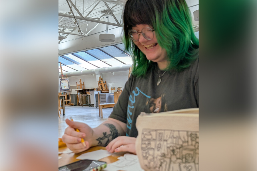 A student with green and black hair smiles as they work in the art studio.