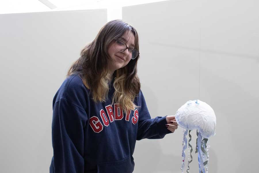 A student in a blue sweatshirt and holds a white jellyfish made of paper.