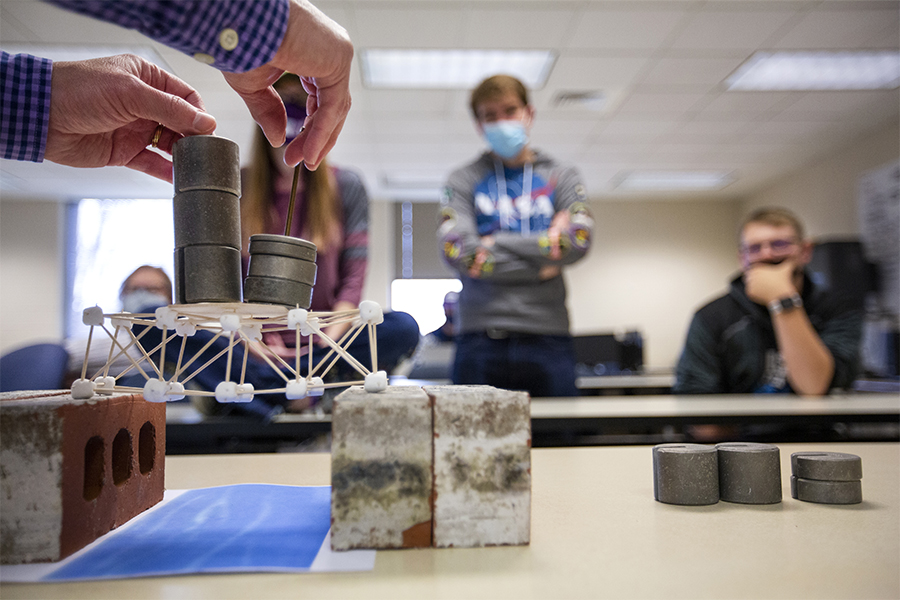 An engineering class creates tests bridges with marshmallows, toothpicks and weights.