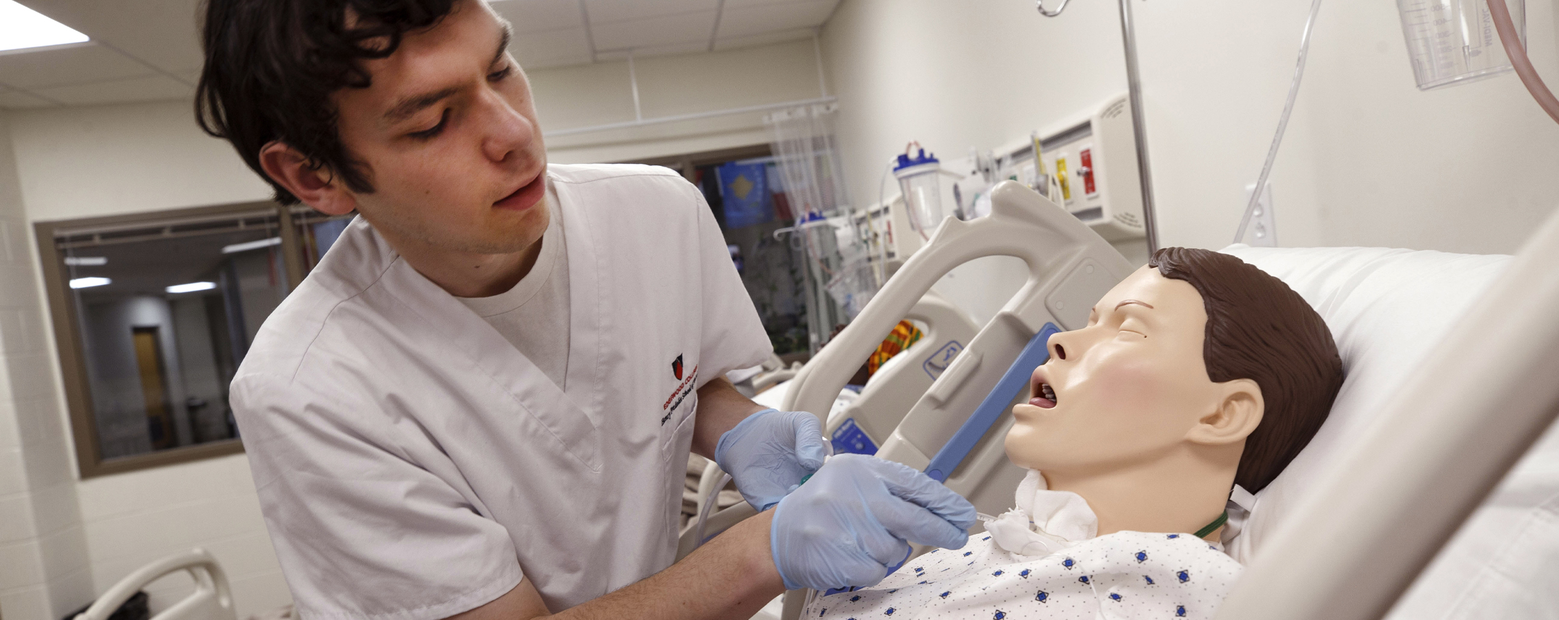 Students stand around a hospital bed and inspect a manikin.