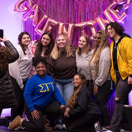 Members of a sorority have their photo taken with a "Galentine's" balloon banner in the background.