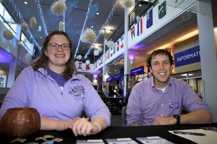 Two people in purple shirts smile at the camera