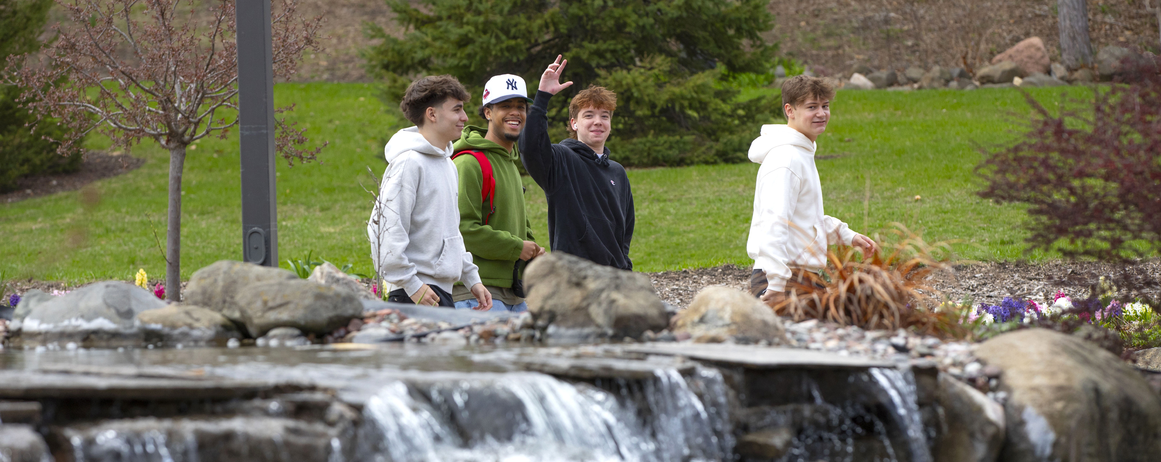 Four students walking past Minneiska Springs smile and wave at the camera.