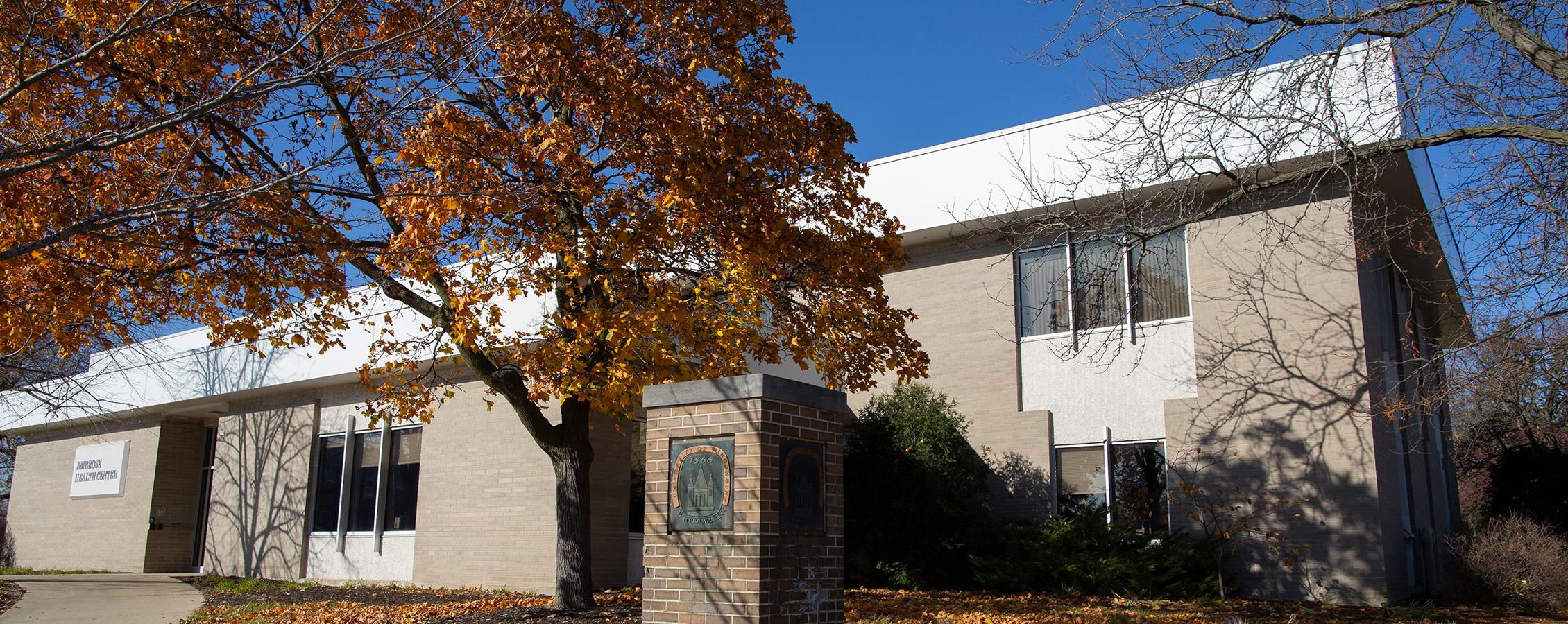 Ambrose Health Center on UW-Whitewater campus with a blue sky in the background and orange tree in the foreground.