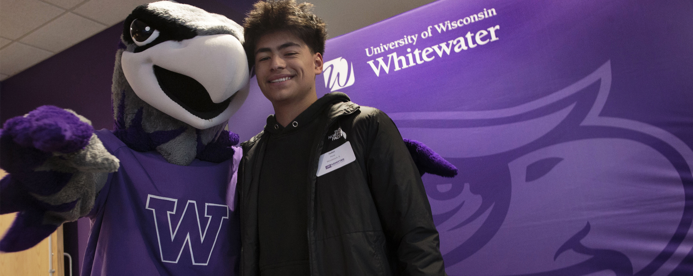 A person poses with Willie Warhawk in front of a purple Warhawk head backdrop.