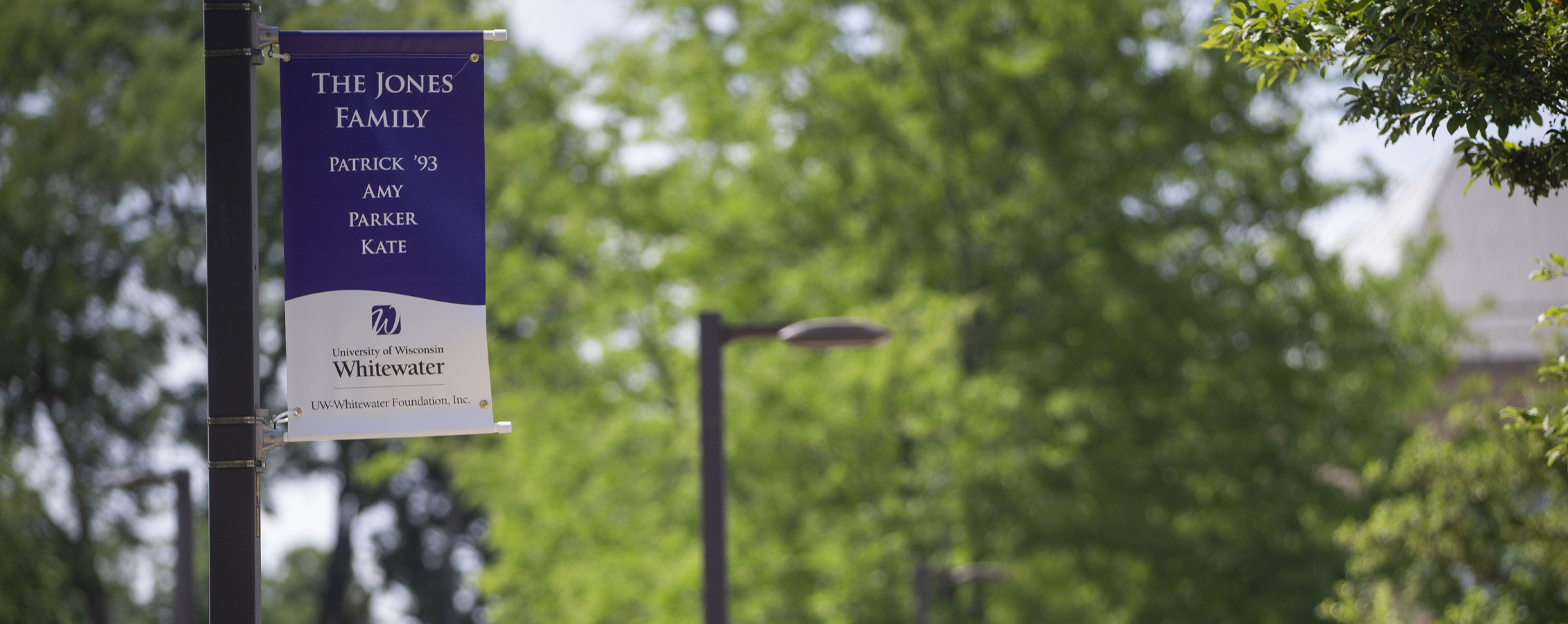 A purple and white sign hangs from a lightpost.