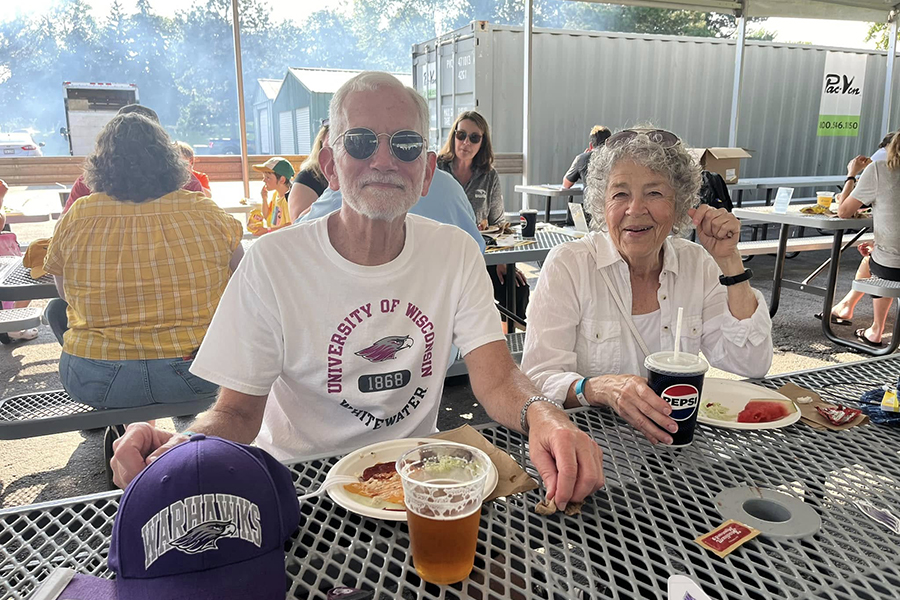 Denny Waldera smiles at the camera while eating outside and wearing a UW-Whitewater tshirt.