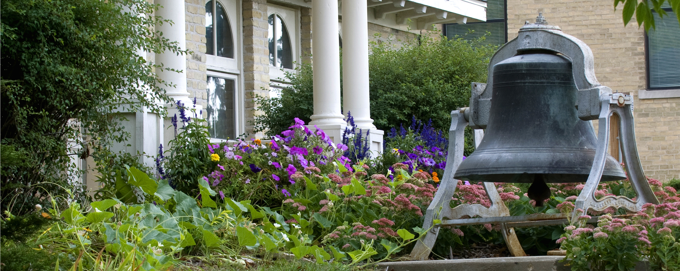 Bell tower outside of the Alumni Center surrounded by flowers.