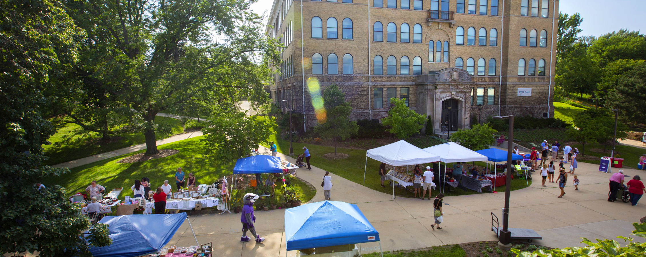 Exterior shot of Hyer Hall: Willie Warhawk and pop tents fill the sidewalk in front of the building.