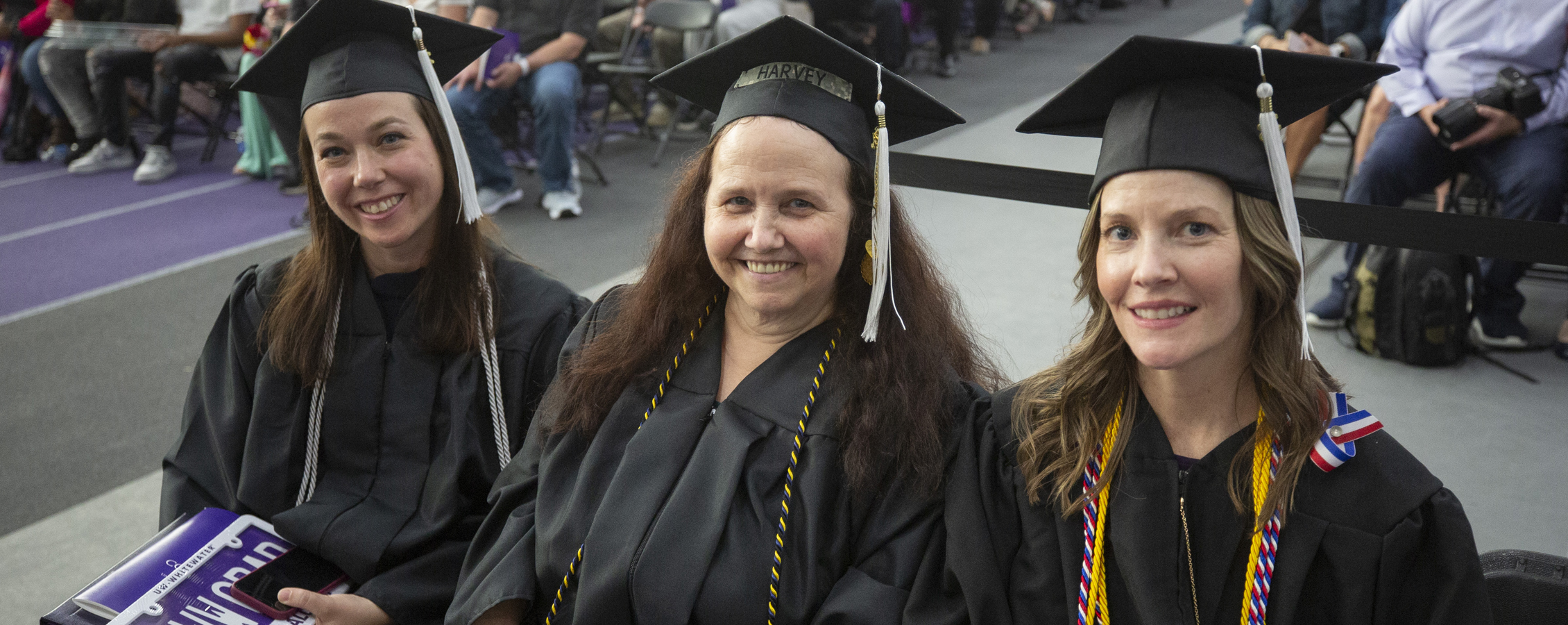 Three adult students wear their cap and gown at graduation.